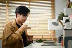年轻的亚洲男人。喝咖啡阅读电子邮件移动PC电脑