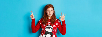 快乐圣诞节快乐的红色头发的人女孩圣诞节毛衣指出手指上角落里显示一年促销批准赞美产品