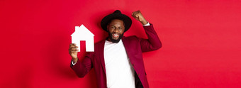 真正的房地产快乐黑色的男人。庆祝购买房子显示纸首页模型提高拳头胜利站红色的背景