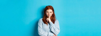 愤怒的红色头发的人女孩使安静显示禁忌手势禁止说话站蓝色的背景毛衣