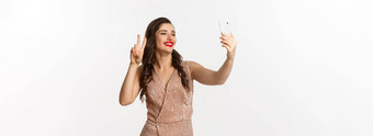 有吸引力的女人奢侈品衣服显示和平标志电话相机采取自拍智能<strong>手机</strong>摆姿势圣诞<strong>节</strong>聚会，派对装站白色背景