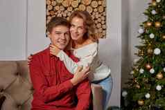 快乐年轻的可爱的夫妇生活房间坐着沙发上圣诞节树