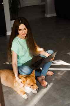 有吸引力的女孩移动PC威尔士矮脚狗狗坐着地板上聊天在线朋友沟通家庭有趣的狗生活方式威尔士威尔士矮脚狗彭布罗克
