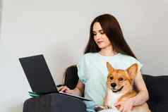 有吸引力的女孩拥抱威尔士矮脚狗狗休息首页女孩国内宠物坐沙发看电影移动PC生活方式威尔士威尔士矮脚狗彭布罗克