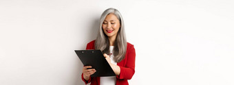 成功的亚洲高级女商人灰色头发采取笔记剪贴板检查企业站白色背景
