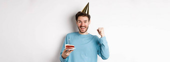 庆祝活动假期概念快乐的年轻的男人。庆祝生日聚会，派对他持有bday蛋糕快乐站白色背景