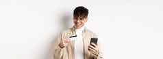 快乐年轻的的家伙眼镜使在线购买塑料信贷卡持有智能手机站白色背景