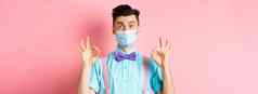冠状病毒医疗保健检疫概念快乐的家伙医疗面具节日蝴蝶结显示好手势使迹象微笑相机粉红色的背景