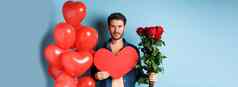 情人节一天浪漫年轻的男人。花束红色的玫瑰心气球微笑带礼物情人情人节日期站蓝色的背景