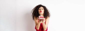 假期庆祝活动概念浪漫的女人红色的衣服庆祝生日吹蜡烛生日蛋糕使站白色背景