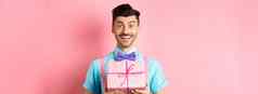 假期庆祝活动概念充满希望的微笑的家伙爱展示可爱的礼物站粉红色的背景