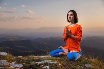 年轻的女人实践瑜伽在户外美丽的山景观背景日落莲花位置纳马斯特冥想放松
