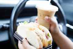 亚洲女人司机持有冰咖啡杯三明治面包吃喝车危险的风险事故