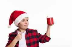 英俊的13岁以下的男孩圣诞老人他指出红色的杯热可可棉花糖孤立的白色背景