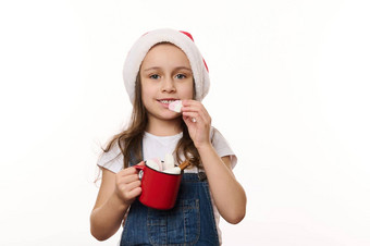 孤立的肖像白色可爱的孩子女孩圣诞老人他持有红色的杯热巧克力吃棉花糖