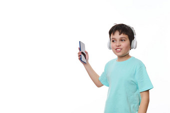 十几岁的男孩持有智能手机舞蹈听音乐立体声耳机孤立的白色背景