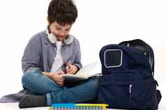 聪明的学生十几岁的男孩无线耳机家庭作业坐着学校袋孤立的白色背景