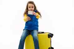 可爱的孩子女孩持有空气票登机通过相机坐着黄色的旅行袋周末度假