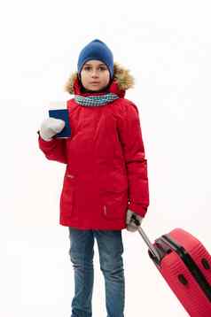 十几岁的旅行者男孩穿红色的派克大衣蓝色的牛仔布牛仔裤走登机通过手提箱白色背景