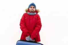 中东十几岁的男孩穿红色的派克大衣皮毛罩持有蓝色的手提箱孤立的白色背景