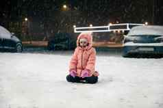 快乐孩子女孩温暖的冬天工作服坐在雪街享受雪晚上走