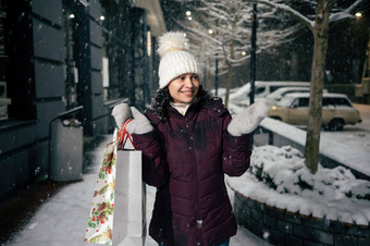 有吸引力的女人购物袋捕获雪花走雪街照亮假期花环