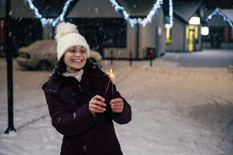 迷人的年轻的女人温暖的冬天衣服灯罗马焰火筒白雪覆盖的街基斯一年的花环