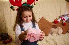 迷人的高加索人女孩穿鹿鹿角希望持有粉红色的心形状的礼物盒子拳击一天圣诞节期