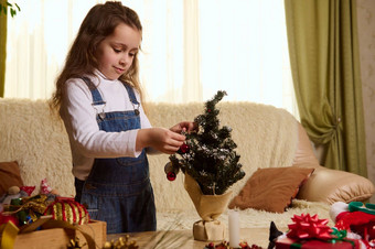 美丽的女孩挂闪亮的球玩具小圣诞节树装修首页冬天假期