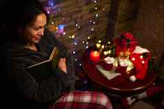 令人愉快的女人读取书烛光坐着表格圣诞节礼物花环