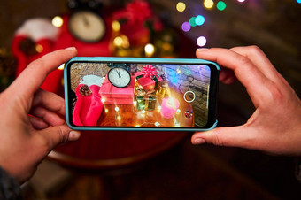 女人手持有智能手机照片圣诞节室内发光的加兰圣诞节礼物