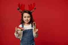 可爱的女孩穿鹿鹿角希望微笑摆姿势糖果狗圣诞节现在红色的背景