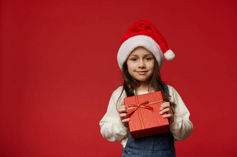 可爱的女孩穿圣诞老人老人他持有红色的礼物盒子圣诞节惊喜孤立的彩色的背景