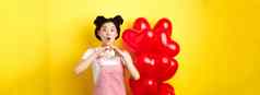 惊讶亚洲女人敬畏显示心手势使爱忏悔情人节一天站浪漫的红色的气球黄色的背景
