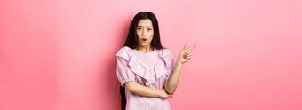 震惊了亚洲青少年女孩衣服指出手指左喘气想知道好奇的相机问题促销站粉红色的背景