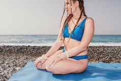 女人海瑜伽中间岁的女人辫子长发绺蓝色的泳装伸展运动普拉提瑜伽席海女健身瑜伽例程概念健康的生活方式