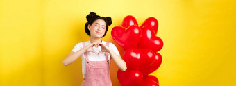 情人节一天概念可爱的亚洲女孩做梦浪漫关闭眼睛显示心手势微笑快乐站红色的浪漫的气球黄色的背景