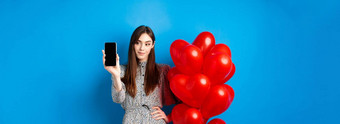 情人节一天漂亮的微笑女人衣服显示空智能手机屏幕站浪漫的气球蓝色的背景