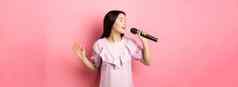 美丽的亚洲女孩执行首歌唱歌麦克风微笑浪漫的站衣服粉红色的背景