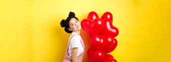 情人节一天概念<strong>时尚</strong>的十几岁的亚洲女孩摆姿势红色的心气球穿装<strong>浪漫</strong>的日期站快乐黄色的背景