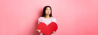 情人节概念孤独的十几岁的亚洲女孩做<strong>梦</strong>爱感觉伤心孤独的情人一天遗憾持<strong>有</strong>大红色的心粉红色的背景