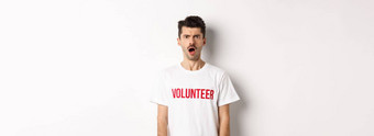 震惊了困惑男人。志愿者t恤盯着相机皱着眉头不高兴站白色背景