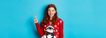 快乐圣诞节快乐的红色头发的人女孩圣诞节毛衣指出手指上角落里微笑兴奋显示一年促销