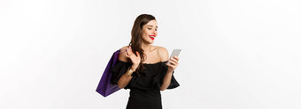 美购物概念华丽的女人优雅的黑色的衣服化妆订单在线智能手机持有袋微笑站白色背景