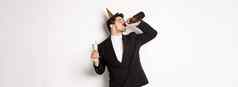 图像英俊的的家伙时尚的西装喝香槟瓶庆祝假期生日聚会，派对喝醉了站白色背景