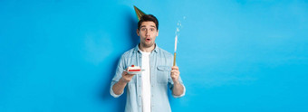 快乐年轻的男人。庆祝生日聚会，派对他持有生日蛋糕微笑站蓝色的背景