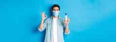 概念科维德流感大流行社会距离满意年轻的男人。医疗面具推荐手洗手液显示标志防腐剂站蓝色的背景