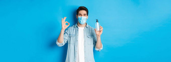 概念科维德流感大流行社会距离满意年轻的男人。医疗面具推荐手洗手液显示标志防腐剂站蓝色的背景
