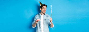 快乐年轻的男人。庆祝生日聚会，派对他持有生日蛋糕微笑站蓝色的背景