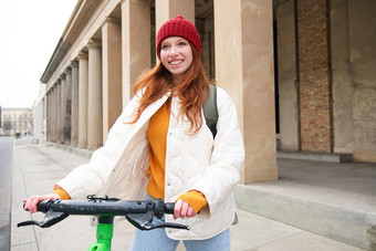 微笑红色头发的人<strong>欧洲</strong>女孩驱动器公共e-scooter旅<strong>游</strong>探讨了城市<strong>游</strong>乐设施城市中心